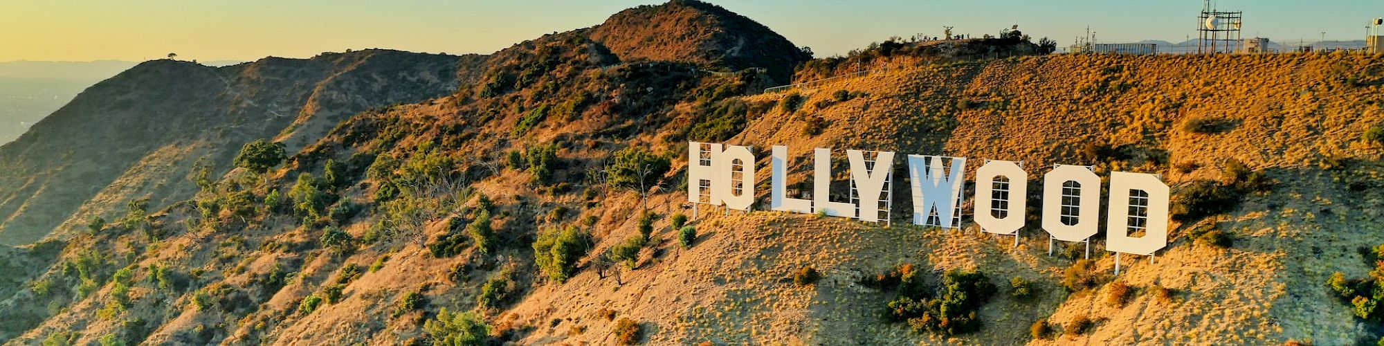 The image shows the iconic Hollywood sign on the hilly landscape with a clear blue sky in the background.