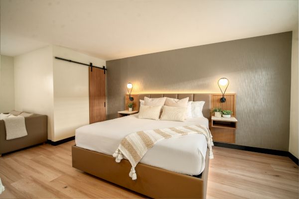 A modern bedroom with a king-sized bed, cozy linens, and bedside lamps, wooden flooring, minimalist decor, and a sliding barn door.