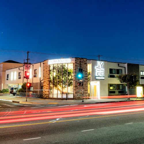 The image shows a corner building at night with illuminated storefronts, streetlights, and light trails from passing vehicles.