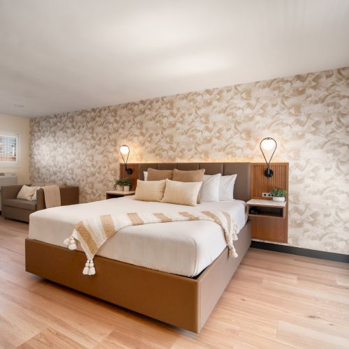 A spacious, modern bedroom features a large bed, elegant lighting, and tasteful decor with hardwood floors and a patterned accent wall.