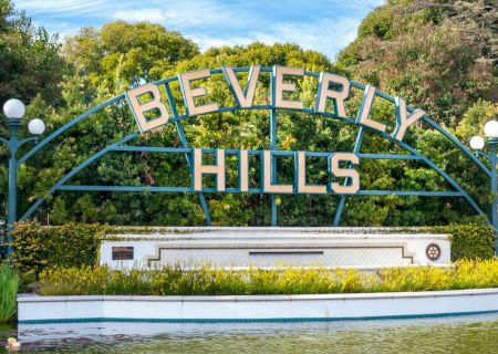 The image shows the iconic Beverly Hills sign, situated in a green park with a water feature and trees in the background, ending the sentence.