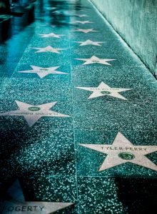 The image shows stars embedded in a sidewalk, likely part of a walk of fame, with names inscribed on each star.